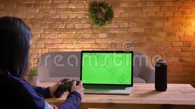 年轻漂亮的女视频博主在笔记本电脑上使用绿色控制台玩视频游戏的特写镜头