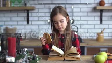 可爱的小女孩穿着格子衬衫，留着长发，在厨房的桌子上吃饼干，<strong>翻阅</strong>一本书