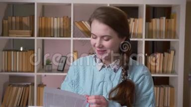 在大学<strong>图书馆</strong>里，一位年轻漂亮的女学生正在读一本书，微笑着看着摄像机