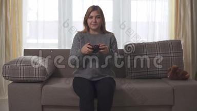 胖女孩在家坐在沙发上玩电子游戏。 胖女人手里拿着操纵杆。 多大号女士休闲