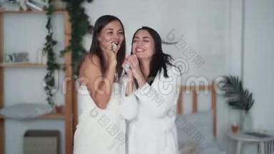 两个穿着白色浴袍跳舞的女朋友，带吹风机唱歌和干头发，笑吧