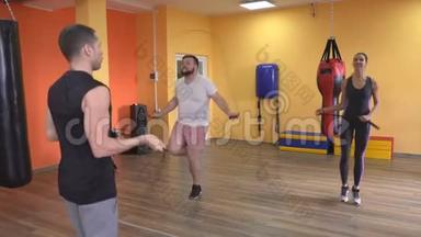 在训练员的监督下，大胡子男人和女孩在健身房里跳一根绳子，在训练拳击前热身