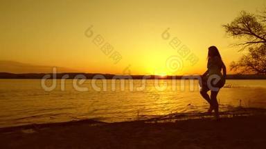 年轻的自由女孩在海边夕阳红下翩翩起舞。 晚上海滩上跳的快乐女人