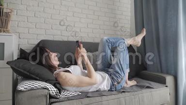 年轻女子躺在沙发上，在智能手机上进行网上购物。 网上购物的概念。