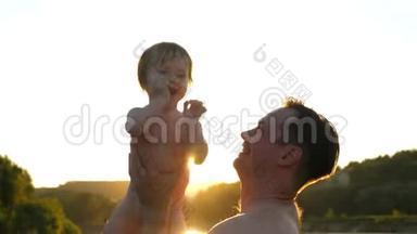 爸爸和小宝宝一起玩，在夏天的时候，在海滩上的日落亮点。 家长把孩子扔了，笑了