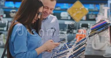 一对已婚夫妇站在现代电子商店智能手机陈列柜附近，选择了一款新的智能手机