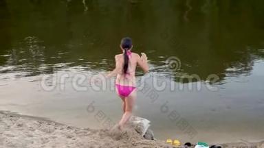 穿着粉红色泳衣，长发的女孩跑下海滩，潜入水中溅起水滴。 少年在沙滩上奔跑