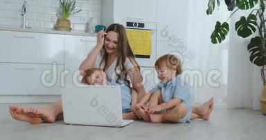 妈妈带着两个小孩坐在一间现代化公寓的地板上，明亮的房间里有一台笔记本电脑。注意