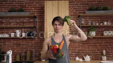 年轻的运动素食主义者拿着西兰花和碗，厨房里有蔬菜。 健康食品和健康食品