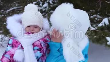 妈妈把小女儿抱在怀里，冬天在公园的白雪上散步，微笑着。 儿童和母亲