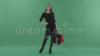 美丽快乐的女人穿着黑色的<strong>小裙子</strong>，摆姿势，用购物袋旋转。 她站在工作室里