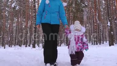 小女孩和她的母亲在公园里的雪冬路上牵手散步。 圣诞节