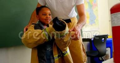 男消防员帮助非裔美国女孩在教室里穿消防制服。 小女生斯密