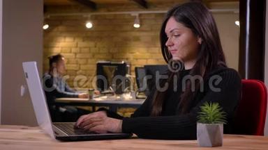 中年黑发女商人在办公室工作时用笔记本电脑打字的特写照片