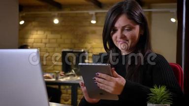 白种人成年女商人的特写肖像，她在平板电脑上滚动着网络，坐在面前微笑