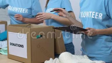 志愿者把捐赠的衣服装在盒子里，主管拿着检查单，小心