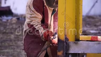 人穿红色和灰色长袍焊接黄色金属施工时戴安全手套和安全面罩.. 安全第一。