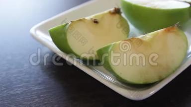 绿色<strong>苹果切片</strong>放在方形的白色盘子里。 摄像机绕着这个向右移动。 特写