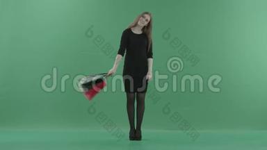 美丽快乐的女人穿着黑色的小裙子，摆姿势，用购物袋旋转。 她站在工作室里