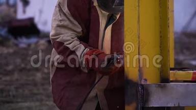 人穿红色和灰色长袍焊接黄色金属施工时戴安全手套和安全面罩.. 安全第一。