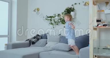 一个长着白色头发和蓝色衬衫的英俊男孩正在沙发上跳跃，慢镜头地看着相机
