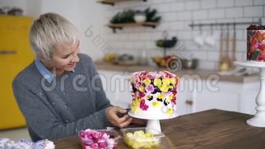 留着短灰头发的女人在<strong>白</strong>色现代厨房装饰着五颜六色的<strong>小白</strong>蛋糕