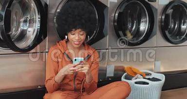 在洗衣店用智能手机微笑的年轻女人。 非裔美<strong>国学</strong>生在智能手机上有好消息。 自我