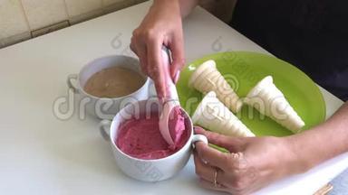一个女人把草莓冰淇淋装满了喇叭。 用冰淇淋勺。 桌子上放着草莓和香蕉的容器
