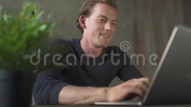 快乐的微笑年轻商人坐在电脑前，在笔记本电脑上打字。 一个英俊的商人发短信