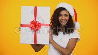 圣诞老人帽子上的一个快乐的混血女孩说：哇，还展示了巨大的礼品盒