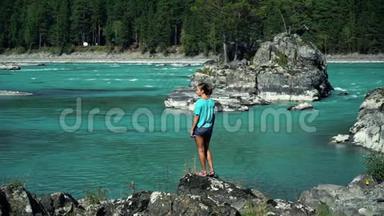 穿着蓝色t恤的年轻女子站在纯净的山河旁，看着江流.. 背面