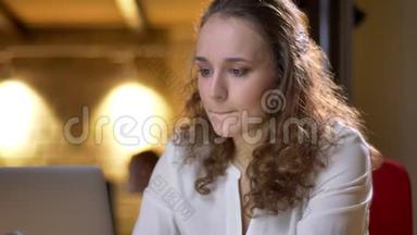一位年轻的<strong>卷发女士</strong>的特写肖像，她专心地用笔记本电脑工作，在办公室里愉快地喝着饮料。