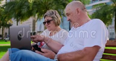 今年夏天，在一个现代化的城市里，快乐的老夫妇坐在长凳上，手提电脑放在摩天大楼的背景上