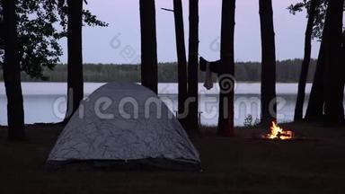黄昏时湖边露营地的景色。 帐篷和火烧的地方被水包围在森林里的树木。 开支
