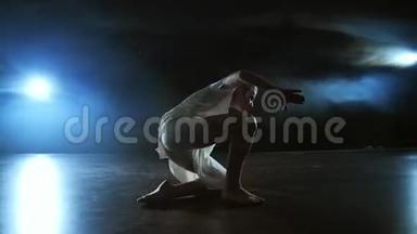 现代舞女穿着白色连衣裙，跳着现代芭蕾，在舞台上用蓝色的烟雾旋转