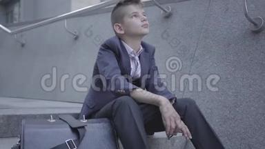 悲伤的衣冠楚楚的男孩坐在街上的楼梯上。 这个男孩<strong>很累</strong>，想做个孩子。 作为儿童