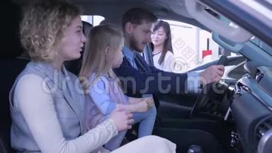 在汽车中心的沙龙里，带着一个个小女孩的幸福家庭在检查汽车的同时高兴买车