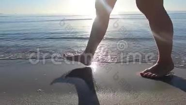 一个年轻女人的腿沿着海岸走着，海浪拍打着她的脚，在黎明时的背光下踩着沙子。