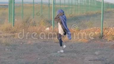 可怜的小女孩徘徊在靠近国界的难民营里，陌生的孩子走在篱笆旁，上面铺着蓝色的毯子
