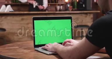 一个穿着休闲紧身衣的年轻人，在带绿色屏幕的笔记本屏幕