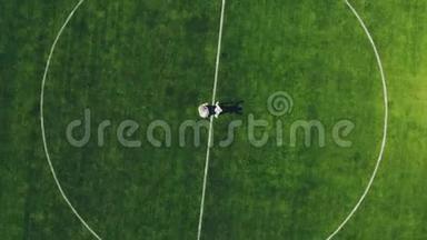 空中视频，从顶部观看，在体育场，在一个绿色足球场的中心，新婚夫妇着婚纱。