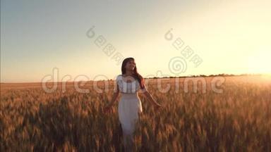 在一个温暖的夏日夜晚，田野里美丽的女孩抚摸着成熟的小麦的耳朵。 穿着白色连衣裙的快乐女孩漫步田野
