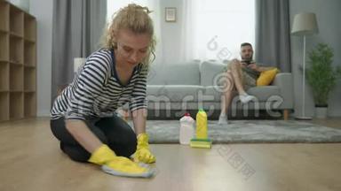 疲惫的妻子打扫地板，丈夫在沙发上玩智能手机
