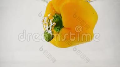 一个新鲜的黄铃状辣椒落入水中，中间有飞溅和气泡