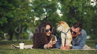 年轻女子带着宠物狗在公园放松时，在智能手机上给<strong>男友</strong>展示有趣的照片，人们都是
