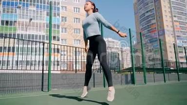 那个女孩在街道上的一个围栏地区参加体育活动。 街头健身<strong>操</strong>.. 蹲着<strong>跳</strong>起来。