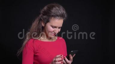 图为一名身着红色衣服的白人妇女微笑着看着黑色背景的智能手机。