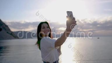 美丽的黑发年轻女子在日出时慢镜头拍摄<strong>靠海</strong>的自拍照片