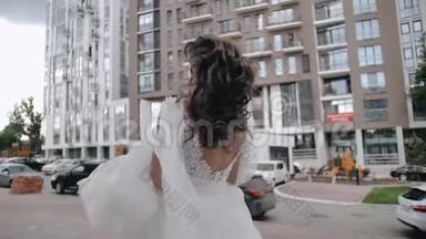 美丽的新娘在城市里走来走去，拿着她的裙子下摆。 漂亮的年轻女孩。