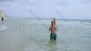 年轻的父亲和他的小儿子在海滩上玩得很开心。 儿子坐在爸爸`肩膀上